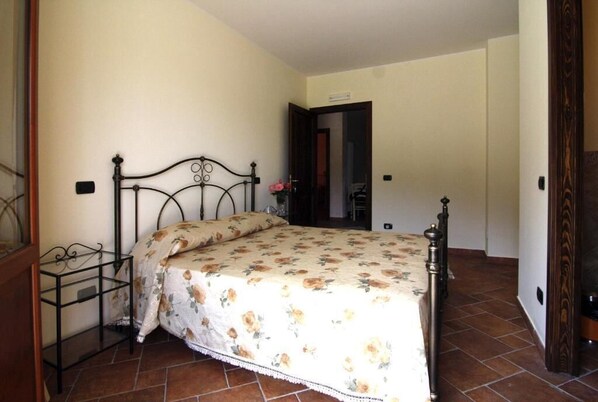 A bedroom with a bed, a nightstand, and a door leading to another room.