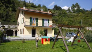 A two-story house with a balcony, a swing set, and a parked car. - La via del sale  (Pignone)