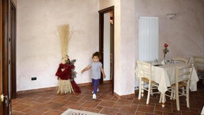 A child walking through a room with a dining table set for two, a broom, and a vase with a red rose. - La via del sale  (Pignone)