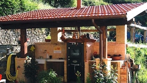 A rustic outdoor kitchen with a brick structure, a tiled roof, and various cooking utensils. - La via del sale  (Pignone)