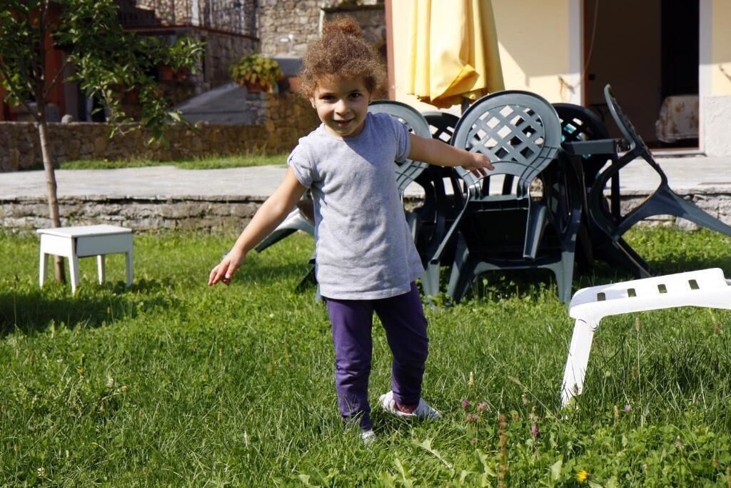 A child standing on grass with outdoor furniture in the background.