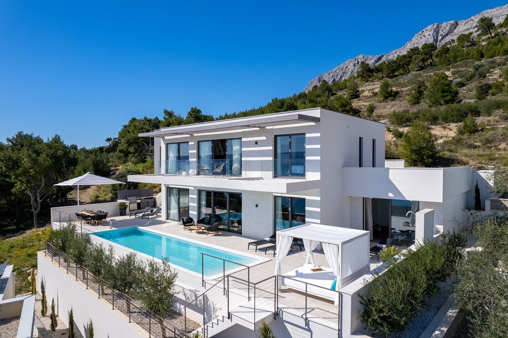 Ein modernes, zweistöckiges Haus mit Swimmingpool, Außenbereich zum Sitzen und Blick auf die umliegende Landschaft.