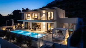 Une maison moderne à deux étages, dotée d’une piscine, d’un espace salon extérieur et offrant une vue sur les montagnes.