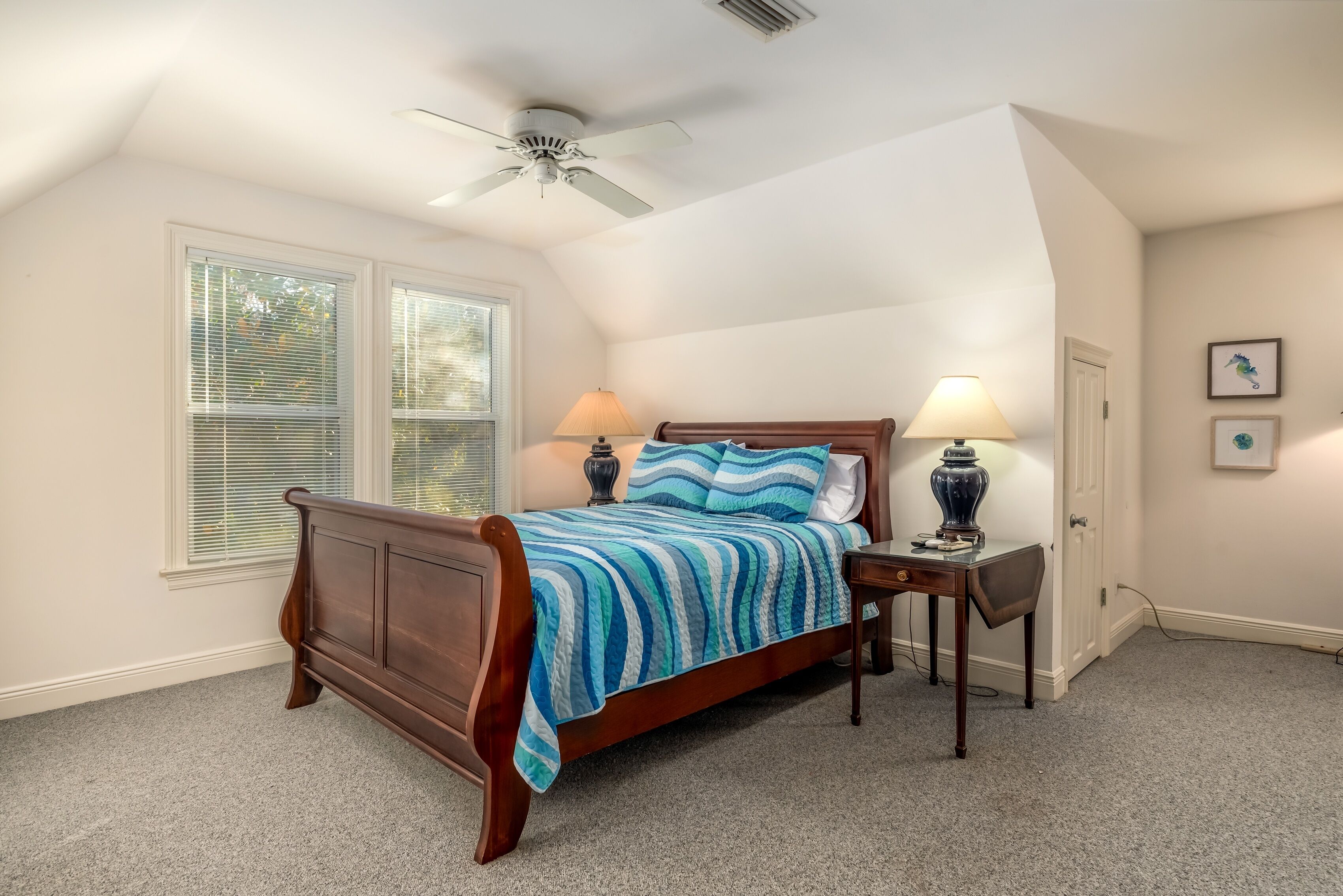 A bedroom with a wooden bed, two bedside lamps, a ceiling fan, and a window with blinds.