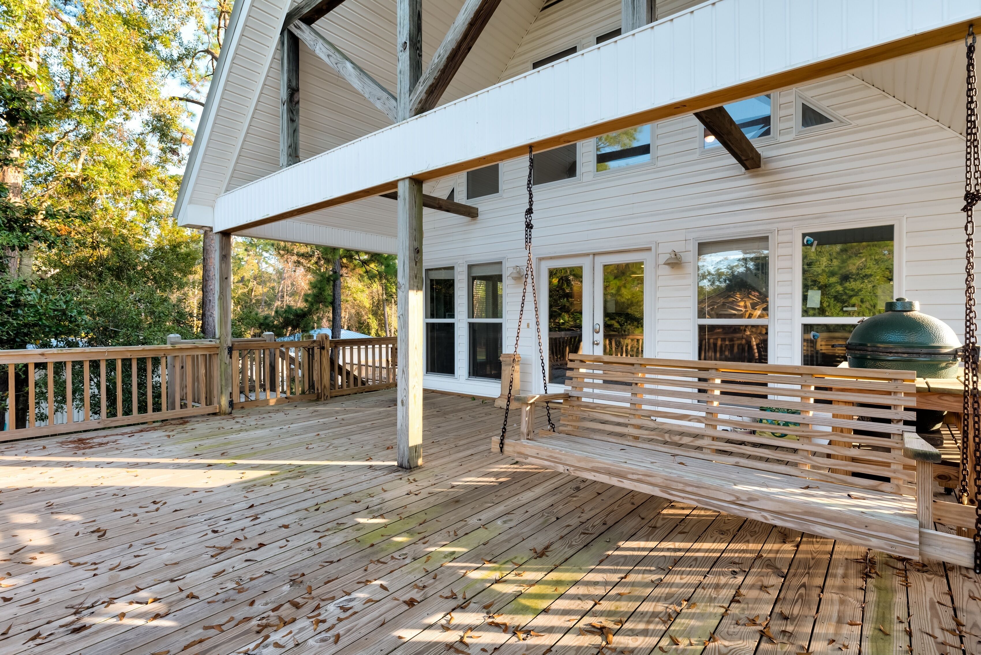 A wooden deck with a swing, white exterior walls, and large windows.