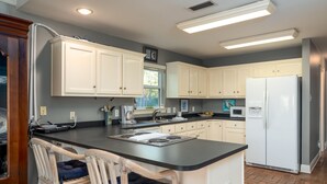 A modern kitchen with white cabinets, a black countertop, a built-in stove, and a white refrigerator. - The Island Spot - 721 Bienville 3 Bedroom Home by RedAwning (Dauphin Island)