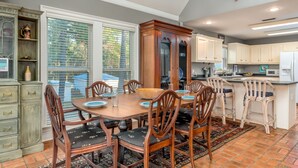 A dining room with a wooden table and chairs, a large fish decoration on the wall, and a view of the outside through the window. - The Island Spot - 721 Bienville 3 Bedroom Home by RedAwning (Dauphin Island)