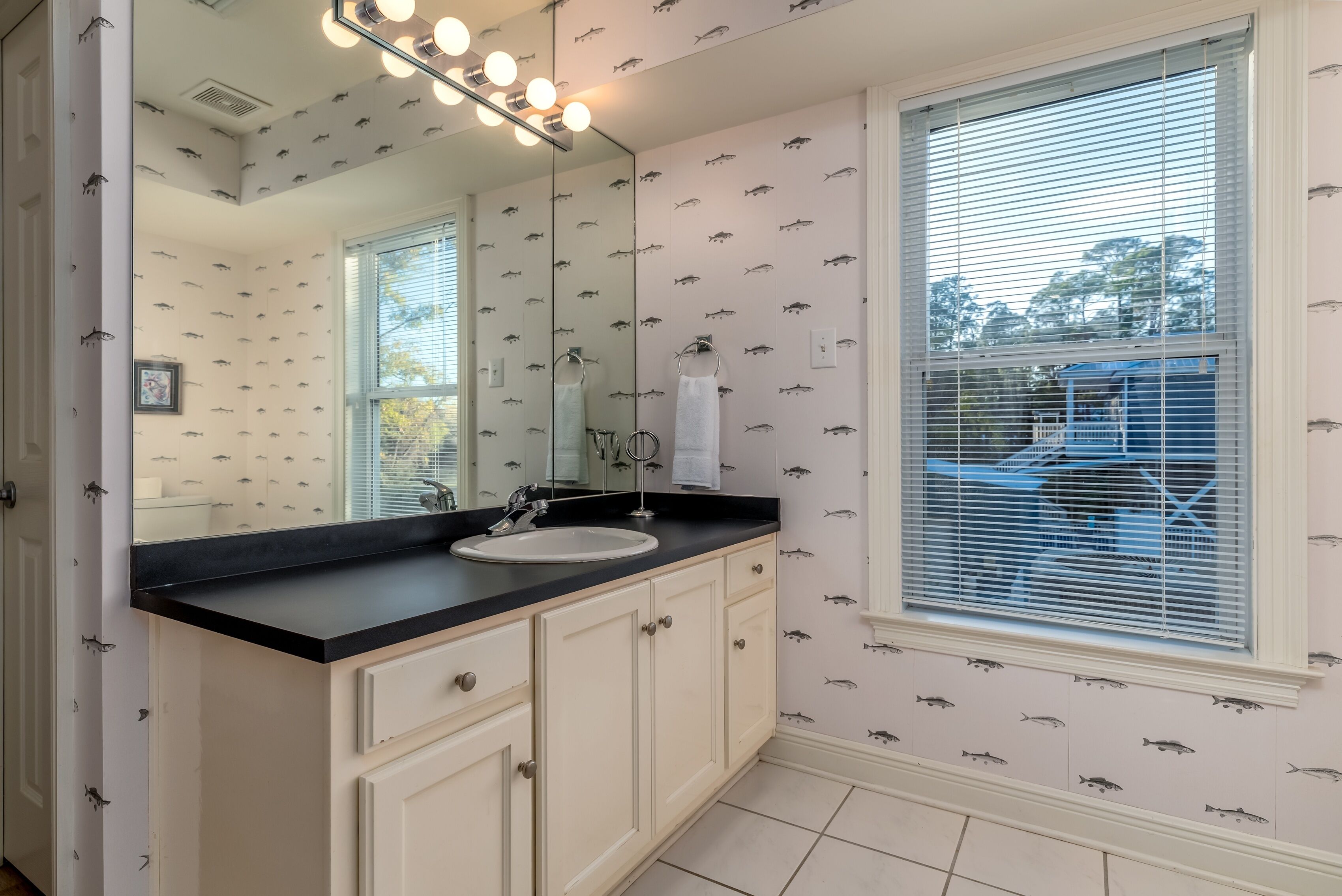 A bathroom with a large mirror, vanity with a sink, and patterned wallpaper.