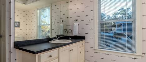 A bathroom with a large mirror, vanity with a sink, and patterned wallpaper.