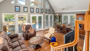 A spacious living room with a high ceiling, large windows, and a view of a deck. - The Island Spot - 721 Bienville 3 Bedroom Home by RedAwning (Dauphin Island)