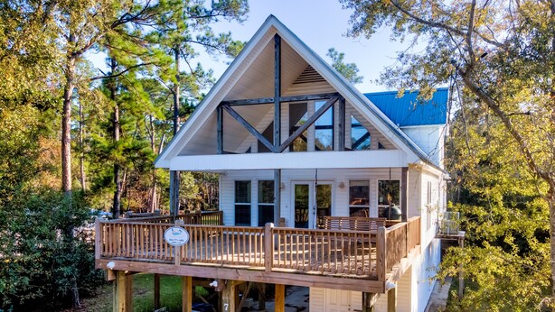 A two-story house with a balcony, surrounded by trees. - The Island Spot - 721 Bienville 3 Bedroom Home by RedAwning (Dauphin Island)