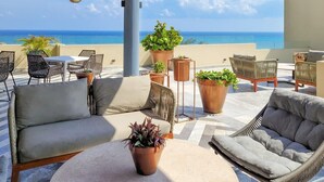 Eine Dachterrasse mit Gartenmöbeln, Topfpflanzen und Blick auf das Meer.