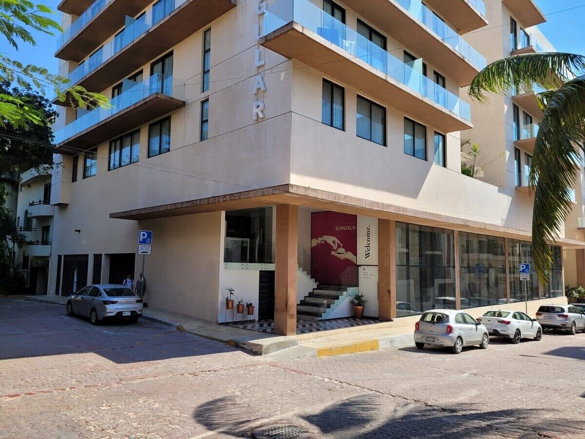 Een meerlaags hotel met een moderne gevel, een opvallende ingang met een rode banner en meerdere auto's ervoor geparkeerd.