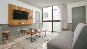 Ein modernes Wohnzimmer mit einem an einer Holzplatte montierten Flachbildfernseher, einem grauen Sofa, einem Couchtisch und einem großen Fenster mit Blick.