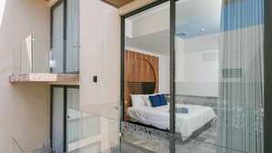 Ein modernes Hotelzimmer mit Glasbalkon, einem Bett mit weißer Bettwäsche und einem Holz-Kopfteil.