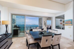 Un espace de repas moderne avec une table et des chaises en verre, une vue sur la mer et un balcon doté d’une balustrade.