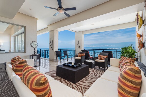 Un vaste balcon offrant une vue sur l’océan, aménagé avec des canapés blancs, des coussins à rayures et une table basse noire.