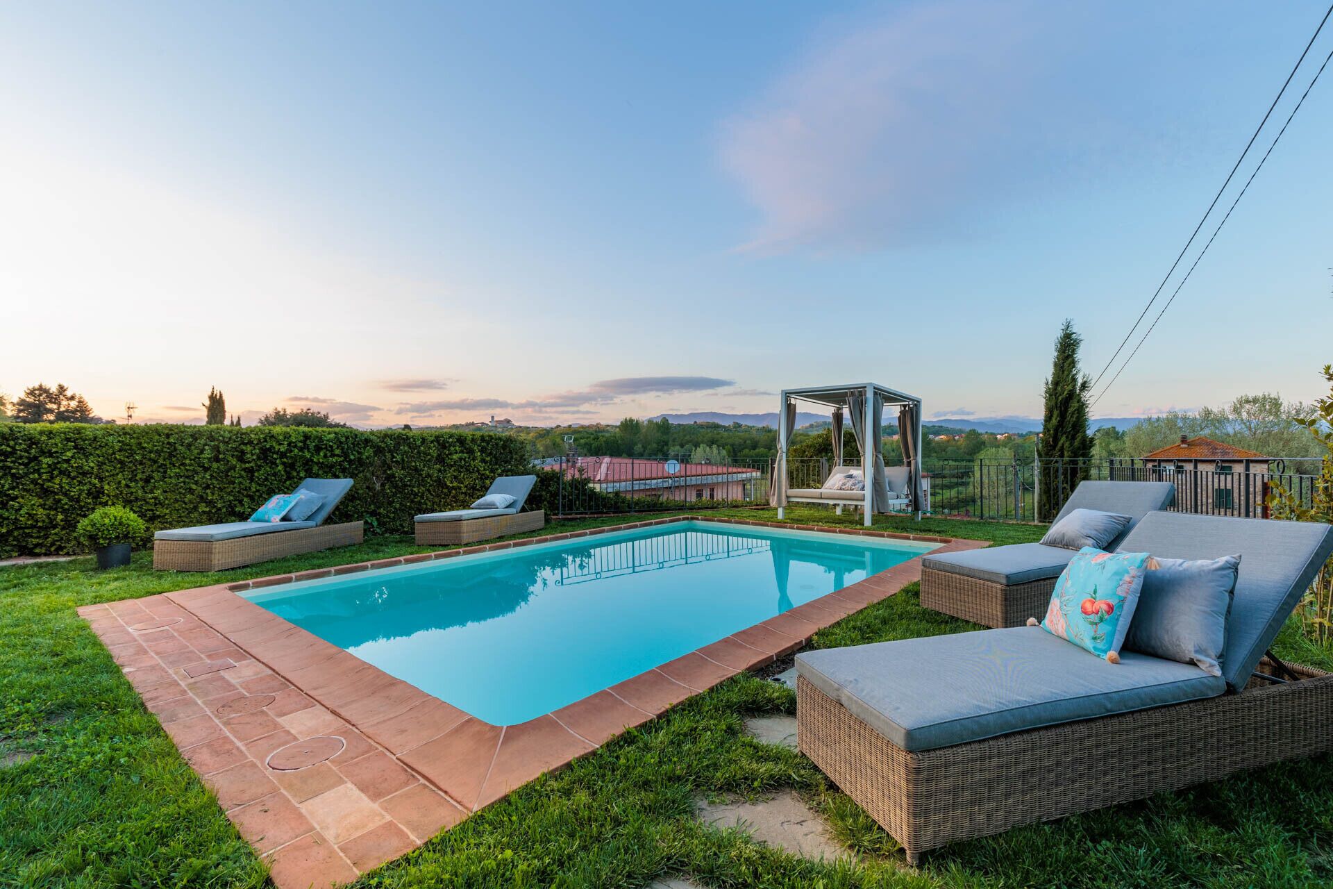 A swimming pool with lounge chairs and a gazebo in a backyard.