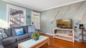 Ein Wohnzimmer mit grauem Sofa, einem Fernseher auf einem Holzständer und Holzboden.