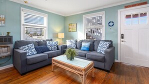 Ein Wohnzimmer mit zwei grauen Sofas, einem Korbtisch und einem Deckenventilator.
