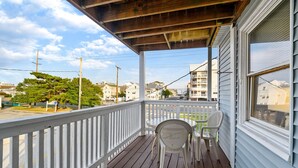 Une terrasse en bois avec une balustrade blanche, deux chaises en plastique et, en arrière-plan, une vue sur des immeubles d’habitation.