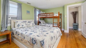 A bedroom with a bunk bed, a bedside table, a window with curtains, and a wall-mounted air conditioner.