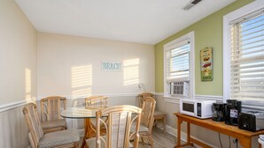A dining area with wicker chairs and a glass table, a white microwave on a wooden table, and a 'BEACH' sign on the wall.