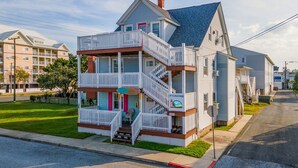 A multi-story beachfront house with a balcony, a porch, and a staircase.