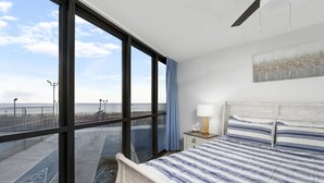 Un dormitorio con un ventanal grande, una cama con ropa de cama a rayas, una mesita de noche y una lámpara de pared.