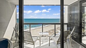 Ein Balkon mit Tisch und Stühlen mit Blick auf einen Strand und den Ozean.
