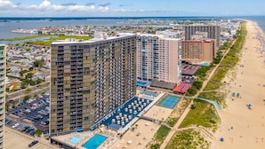 A high-rise hotel with multiple floors, a swimming pool, and a beach area with umbrellas. - Golden Sands 1901 by Seaside Vacations & Sales (Ocean City)