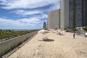A beach with umbrellas, lounge chairs, and a fence.