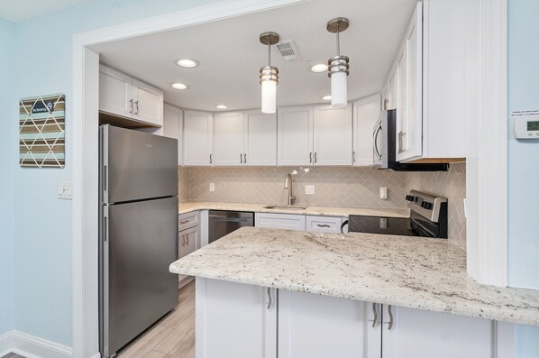 A modern kitchen with white cabinets, a stainless steel refrigerator, a granite countertop, and pendant lighting.