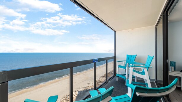 A balcony with a view of the beach, turquoise chairs, and a glass table. - Fabulous Oceanfront condo w/ pools by Seaside Vacations & Sales (Ocean City)