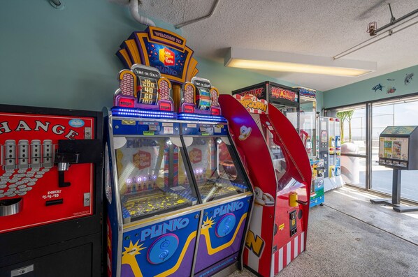 Una hilera de juegos de arcade, incluyendo 'Plinko' y 'Hot Stuff', en un espacio interior bien iluminado.