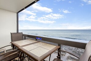 A balcony with a table and chairs, overlooking a beach with a clear sky.