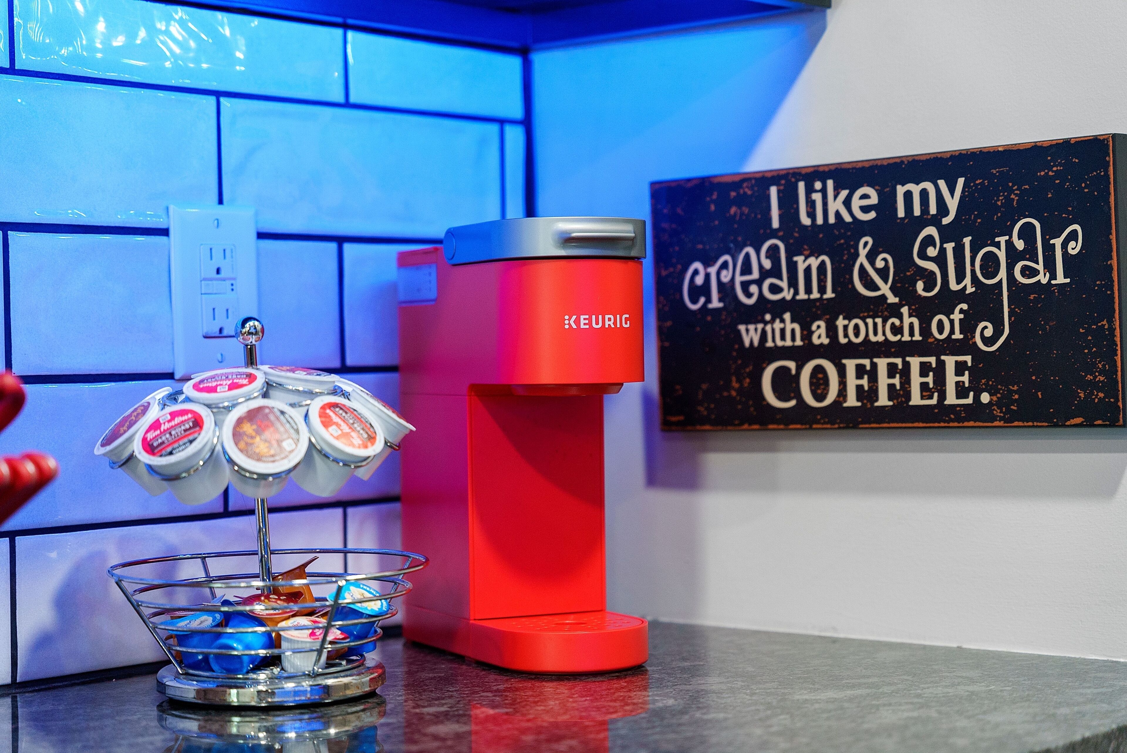 Una macchina da caffè rossa Keurig, un contenitore di panna e zucchero, e un cartello con su scritto 'Mi piace la mia panna e lo zucchero con un tocco di caffè'.