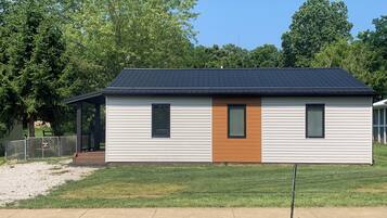 A single-story mobile home with a dark roof, a central door, and two windows on the side.