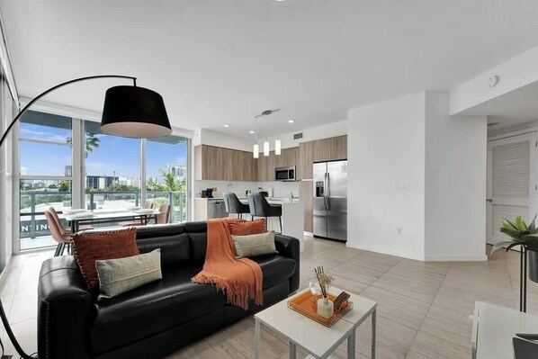 Ein modernes Wohnzimmer mit einem schwarzen Ledersofa, einem Couchtisch mit Tablett und einem großen Fenster mit Blick auf die Stadt.