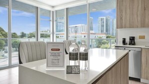 A modern hotel room with a large window, a kitchen area, and a desk with a sign indicating a parking pass and keycard.