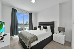 Ein modernes Hotelzimmer mit einem großen Bett, einem Flachbildfernseher und einem Balkon mit Vorhängen.