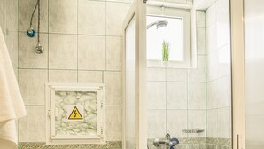 Ein Badezimmer mit Toilette, einer Duschkabine mit Glastür und einem kleinen Fenster mit Pflanze.
