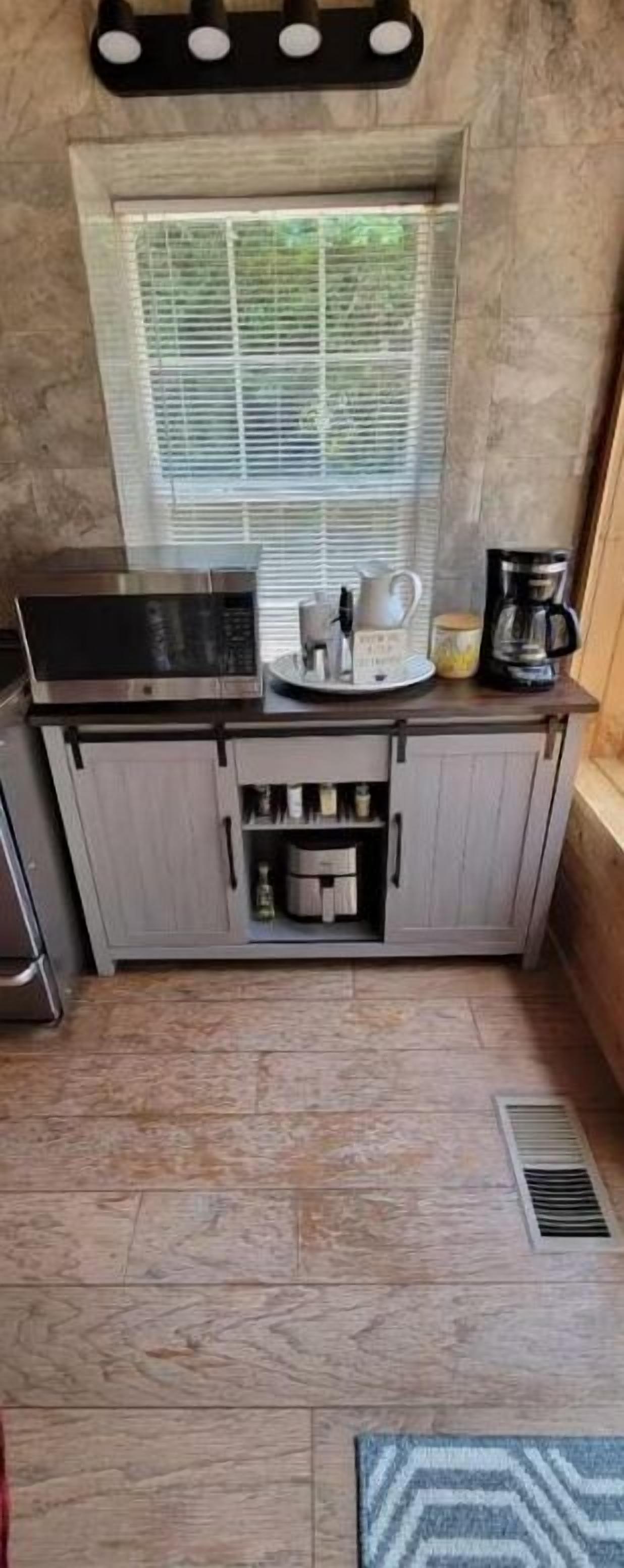 A compact kitchen with a microwave, coffee maker, and a window with blinds.