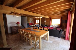 Interior em madeira com mesa de jantar, cadeiras, um sofá e uma televisão.