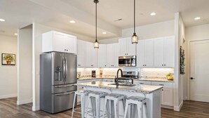 A modern kitchen with white cabinets, stainless steel appliances, and a central island with bar stools.