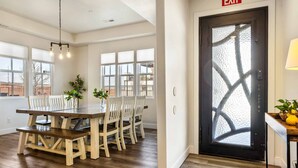 A dining area with a wooden table and chairs, a chandelier, and large windows.