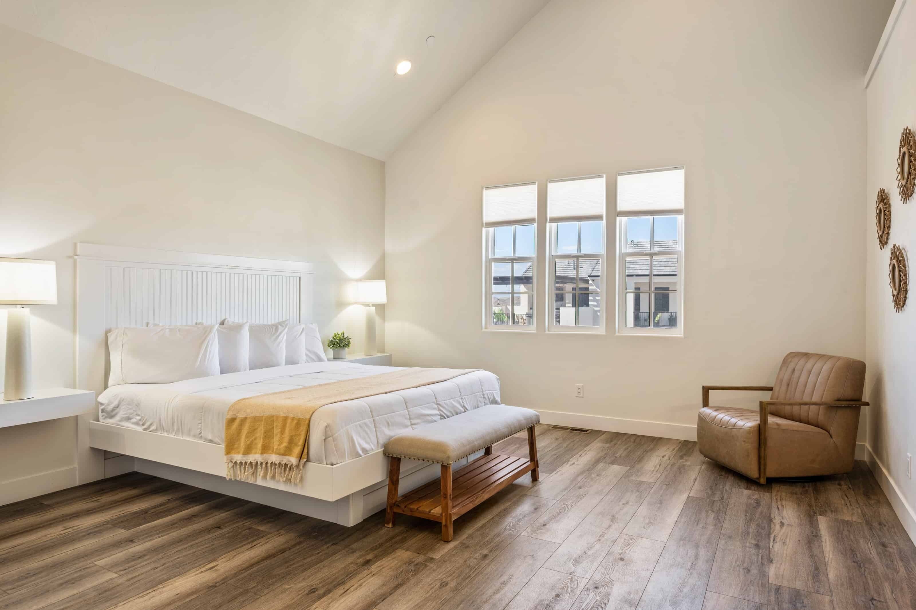 Een ruime slaapkamer met een groot bed, een bankje, een stoel en uitzicht op de stad door grote ramen.
