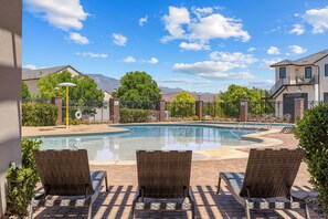 A swimming pool with lounge chairs, a brick wall, and a mountain backdrop.