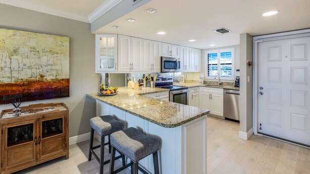 A modern kitchen with white cabinets, a granite countertop, and a large island with bar stools. - NEW Salt Water Pool and Sun Deck Steps to Vanderbilt Beach Water Views (Naples)