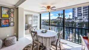 A dining area with a table and chairs, a ceiling fan, and a large window with a view of a marina and buildings. - NEW Salt Water Pool and Sun Deck Steps to Vanderbilt Beach Water Views (Naples)